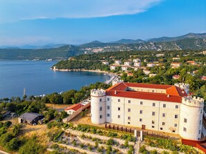 Un château avec un toit rouge, entouré de verdure et bordé par un plan d’eau.