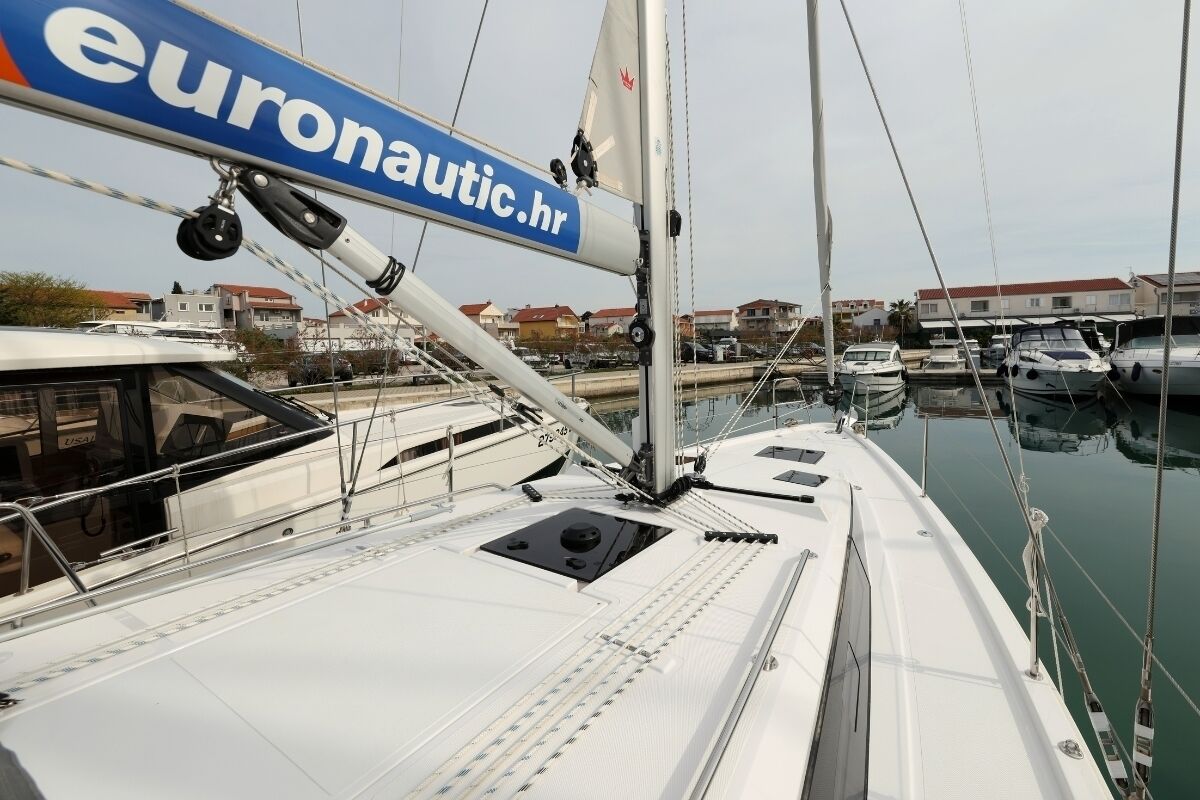 A marina with boats docked, a sailboat with a 'euronautic.hr' sign, and a calm water body.