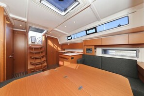 Ein Bootsinnenraum mit Esstisch, Sitzgelegenheiten, einer Steuerung und Fenstern.
