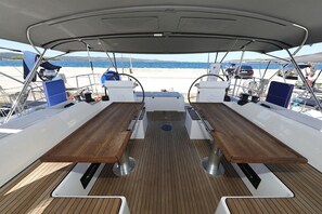 Een dek van een boot met een tafel in het midden, zitplaatsen en uitzicht op zee.