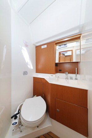 Een kleine badkamer met een wit toilet, houten kastjes, een wastafel met kraan en een spiegel.