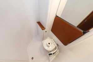 Een kleine badkamer met een wit toilet, een houten wastafelmeubel en een witte wasbak.