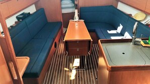 A compact interior with a central table, two blue cushioned seating areas, a small sink, and a television mounted above the table. - Sun-Kissed Sailing Adventure in Zadar, Croatia (Drage)