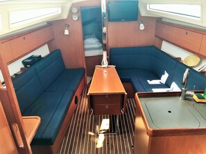 A compact interior with a central table, two blue cushioned seating areas, a small sink, and a television mounted above the table. - Sun-Kissed Sailing Adventure in Zadar, Croatia (Drage)