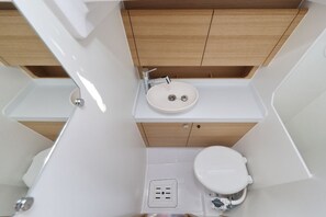 Een kleine badkamer met een witte wastafel, een houten opbergmeubel en een toilet.