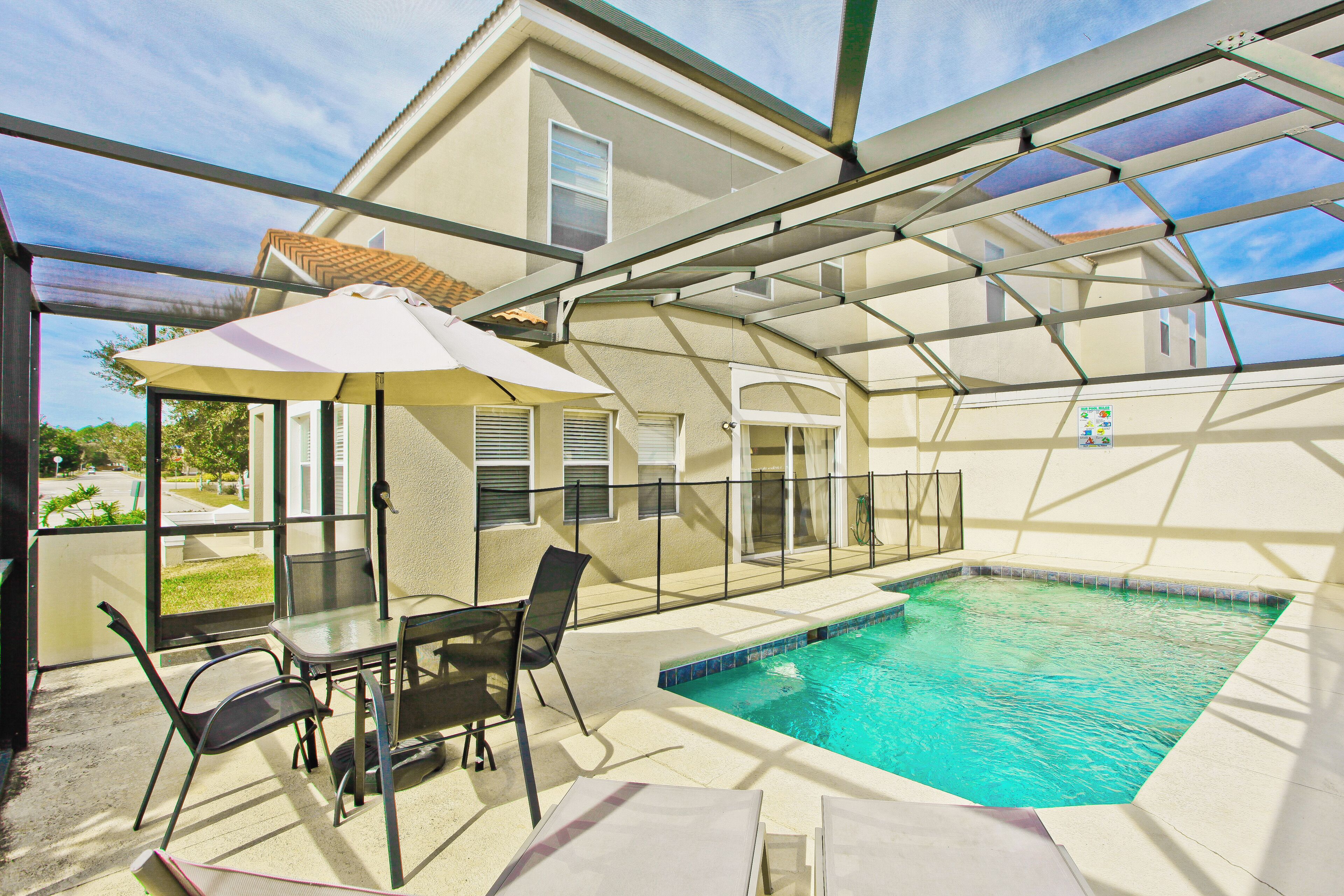 A covered outdoor swimming pool with a glass enclosure, a table with chairs, and a patio umbrella.