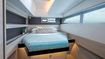 Une chambre à coucher compacte et moderne, avec un lit placé au centre, juste sous un puits de lumière, une petite table de chevet et une fenêtre offrant une vue sur l’extérieur.