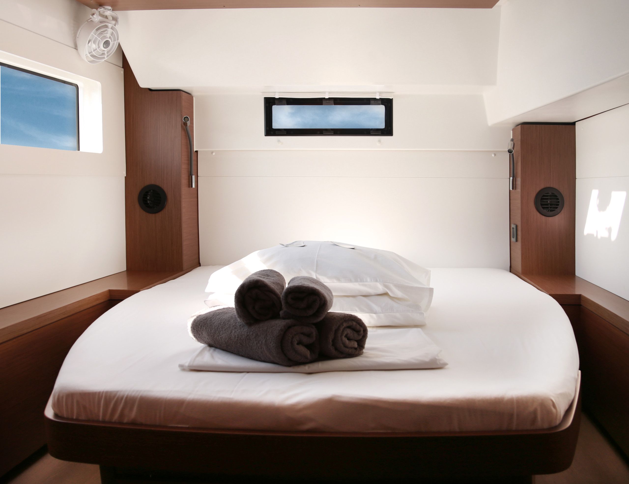 Un lit simple avec un matelas et des oreillers blancs, une petite fen être donnant sur un paysage agréable et un ventilateur de plafond.