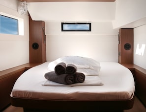 A single bed with a white mattress and pillows, a small window with a view, and a ceiling fan. - Sun-Kissed Sailing Adventure in Islas Sarónicas (Piraeus)