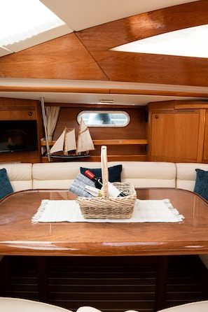 A yacht interior with a round dining table, cushioned seating, a television, and a model sailboat. - Sun-Kissed Sailing Adventure in the Ionian Islands, Lefkada (Lefkada)