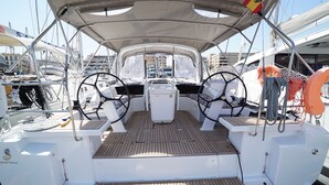 Convés de barco com leme, dois assentos, uma mesa e um toldo.