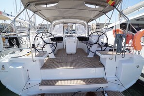 Ein Bootsdeck mit Steuer, zwei Sitzen, einem Tisch und einem Sonnensegel.