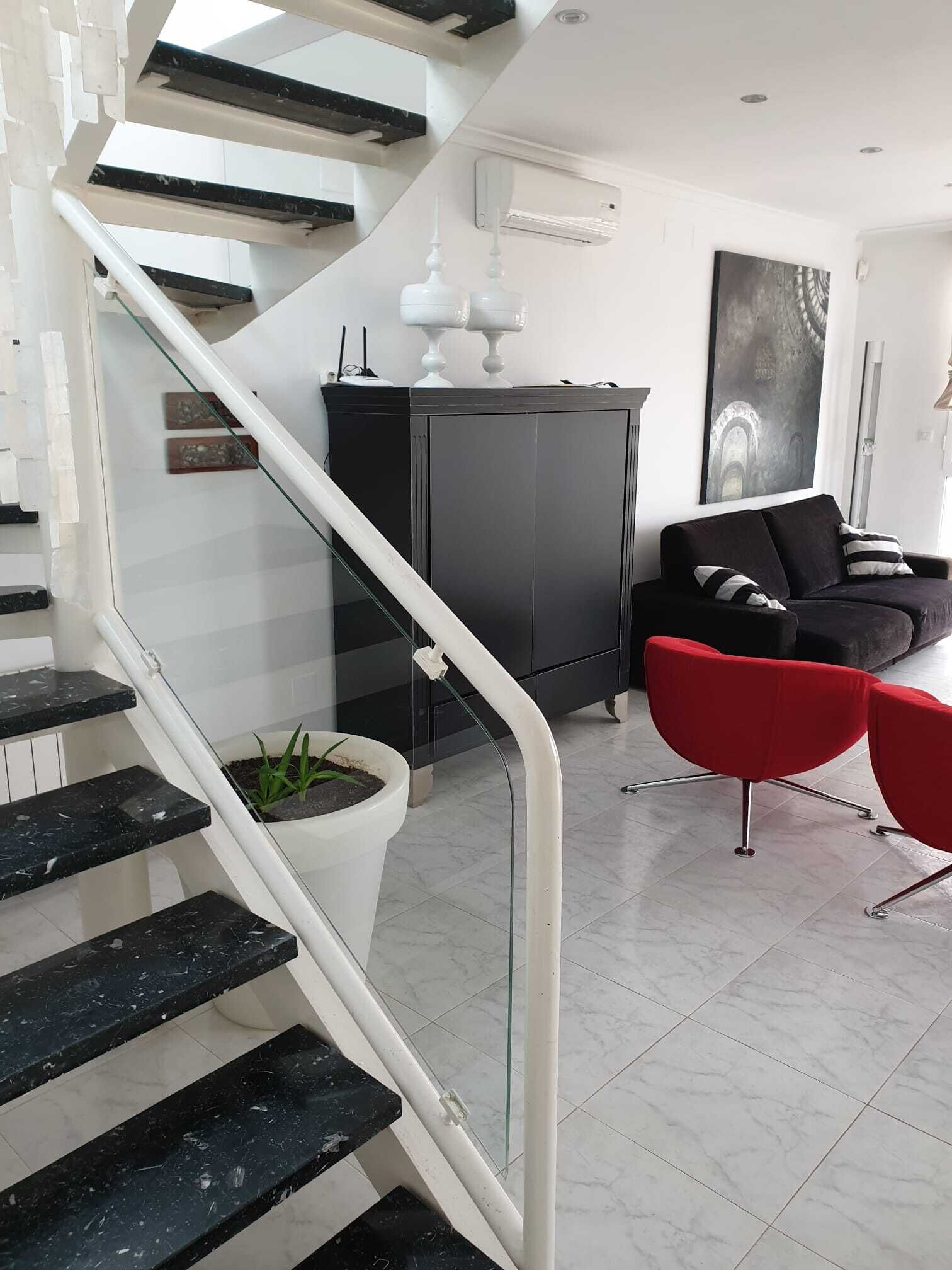 Een moderne woonkamer met een trap, een zwarte kast, een rode stoel en een potplant.