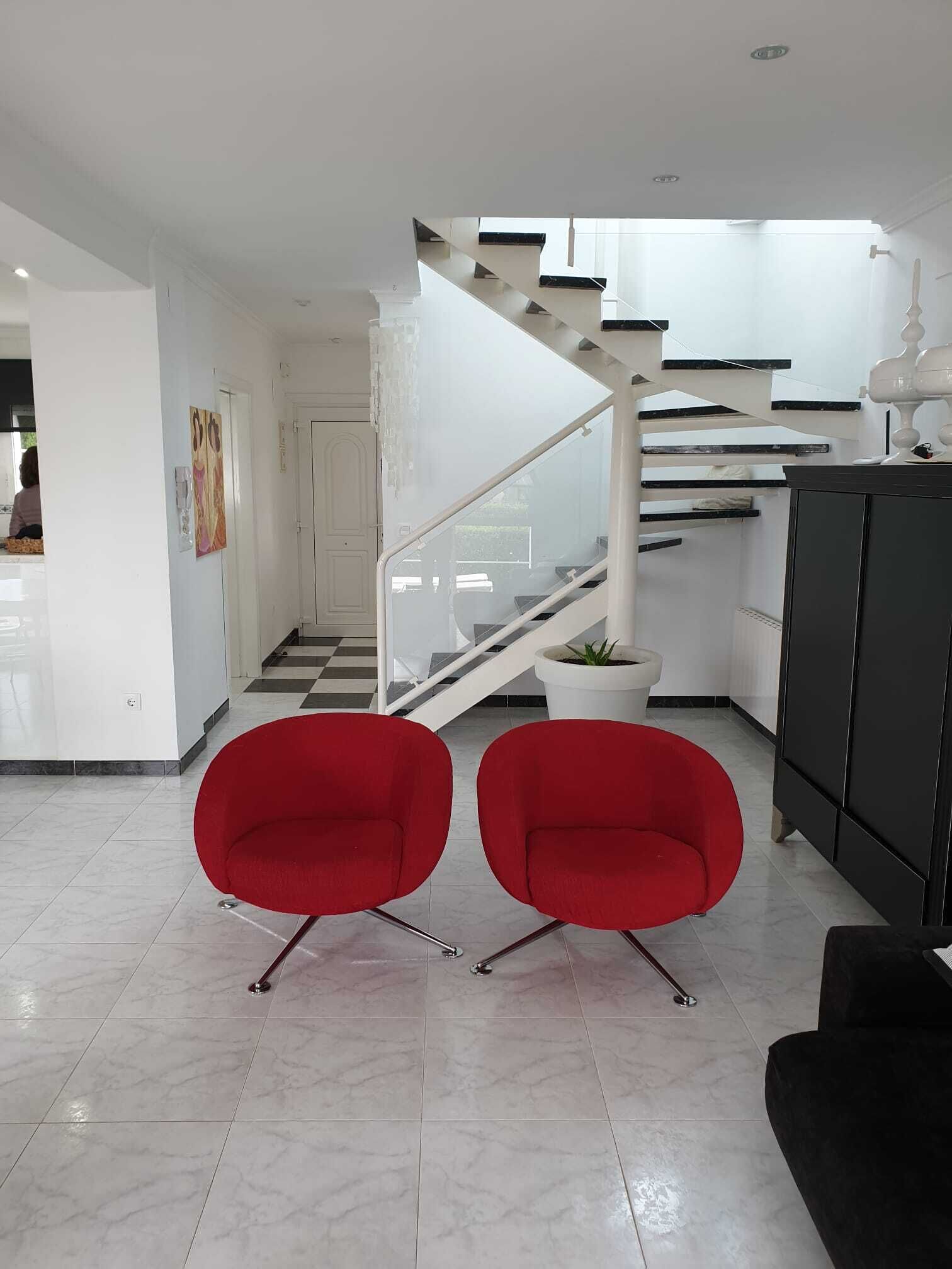 Een modern interieur met een trap, twee rode stoelen, een zwart kastje en een potplant.