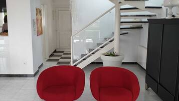 Een modern interieur met een trap, twee rode stoelen, een zwart kastje en een potplant.