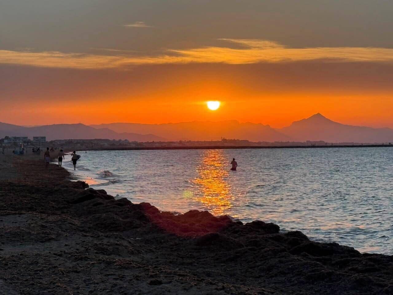 Een zonsondergang boven een wateroppervlak, met een berg op de achtergrond.