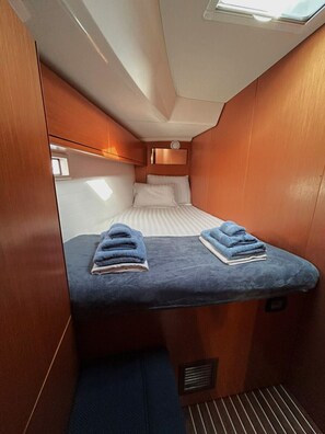 A compact cabin with a bed, two blue towels, and a small window. - Sun-Kissed Sailing Adventure in Islas Sarónicas (Alimos)