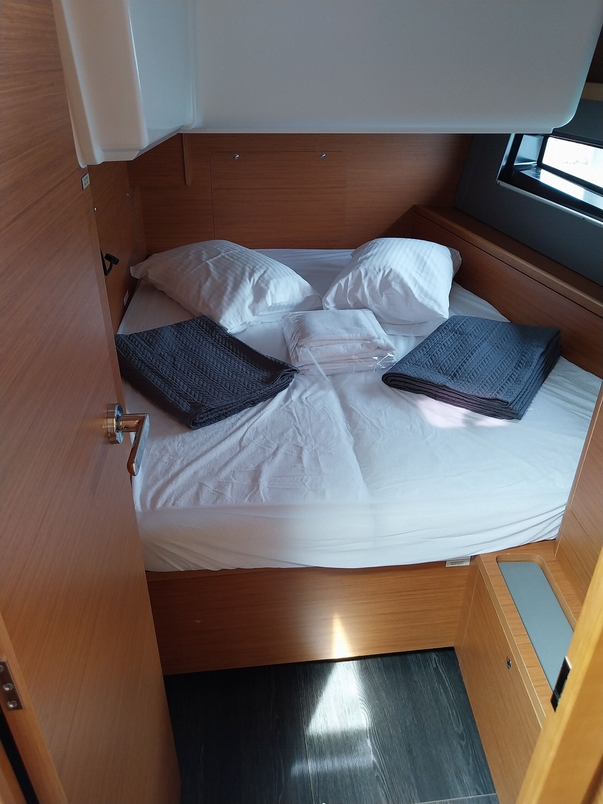A compact bed with white bedding and two folded blankets, a wooden headboard, and a small window.