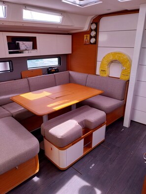 Ein gemütliches Bootsinnere mit Holztisch, gepolsterten Sitzen, einem kleinen Regal mit Gegenständen und einem Fenster mit Meerblick.