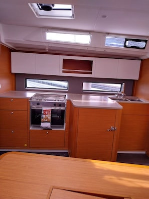 A compact kitchen with a stove, oven, and sink, wooden cabinets, and overhead lighting.