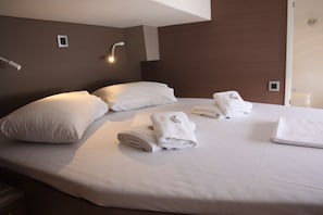 A neatly made bed with pillows and folded towels, a bedside lamp, and a wall-mounted light fixture in a hotel room. - Sun-kissed Sailing Adventure in the Ionian Islands (Preveza)