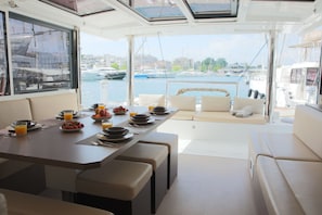 A yacht interior with a dining area, seating, and a view of the marina. - Sun-kissed Sailing Adventure in the Ionian Islands (Preveza)