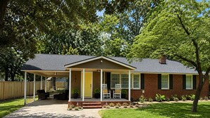 A single-story brick house with a covered porch, a front door, and a small garden area.