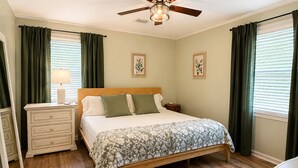 A bedroom with a bed, a nightstand, a ceiling fan, and two windows with curtains.