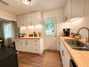 Une cuisine avec des meubles blancs, un plan de travail en bois, un évier et une porte avec une fenêtre.