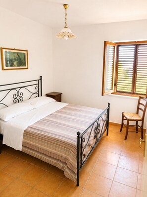 A bedroom with a bed, a nightstand, a chair, a window with blinds, and a hanging light fixture. - Dimora del Lago Tiberino e della Foresta Fossile (Dunarobba)