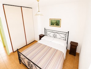 A bedroom with a bed, a nightstand, a wardrobe, and a painting on the wall.