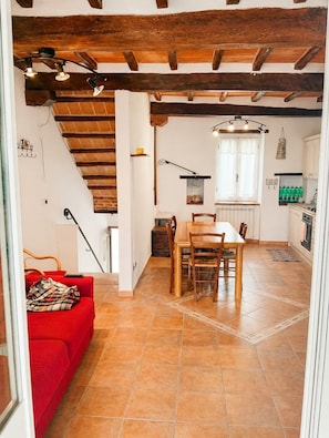 A dining area with a wooden table and chairs, a red sofa, and a kitchen in the background.