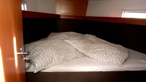 Ein Stockbett mit gemustertem Bettbezug und Kissen, ein Holz-Kopfstück und ein kleines Fenster darüber.