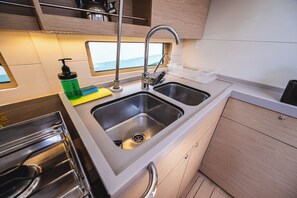 A compact kitchen with a double sink, stainless steel appliances, and a view through a window. - Sun-Kissed Sailing Adventure in the Ionian Islands, Lefkada (Lefkada)