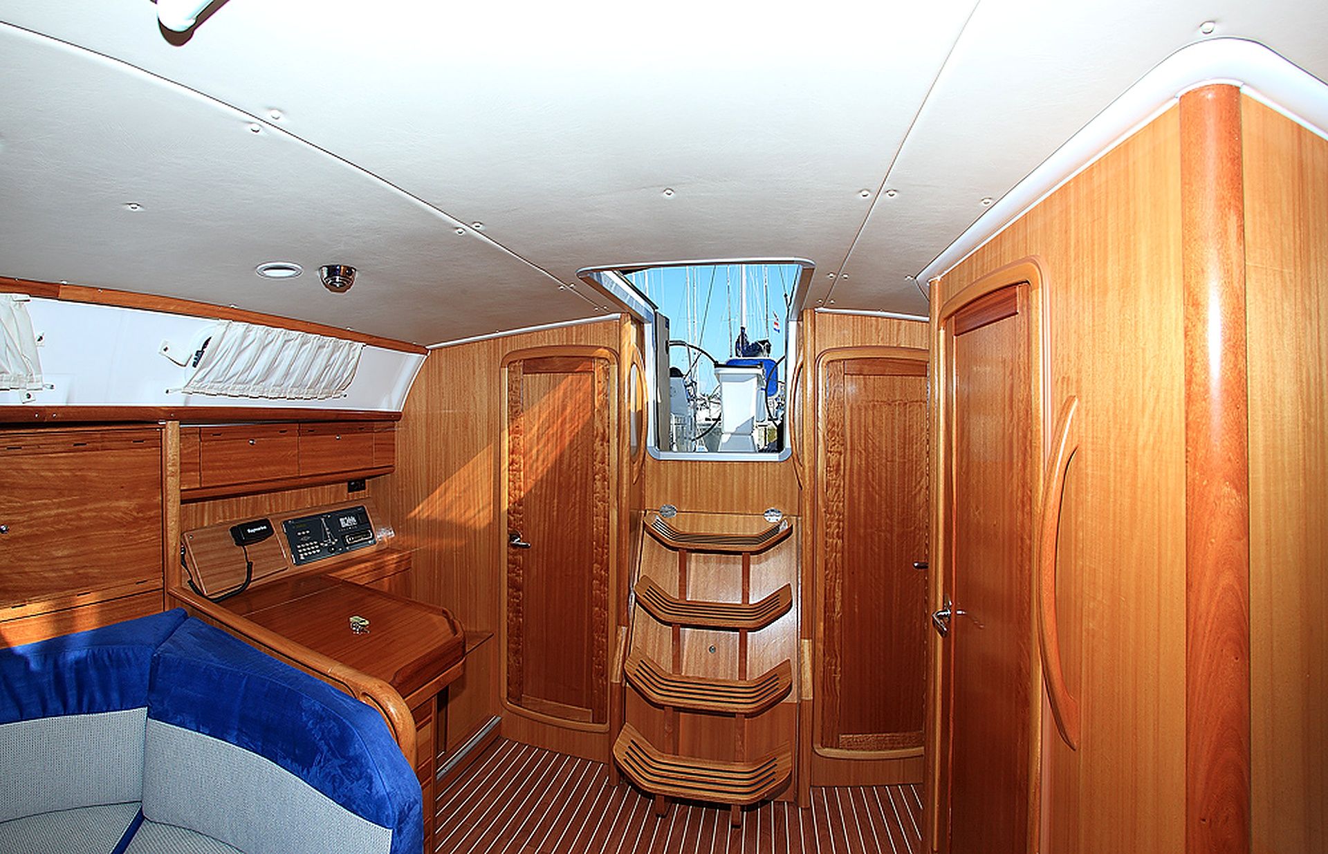 A compact, well-lit cabin with wooden paneling, a control panel, and a window offering a view of the deck.