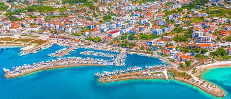 Vista aérea de un pueblo costero con un puerto deportivo, edificios residenciales y una playa.
