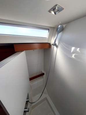 A compact bathroom with a shower, a skylight, and a wooden shelf.