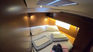 A compact room with a bed, pillows, a blanket, and a pair of shoes.