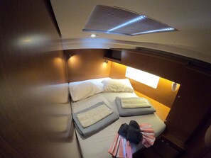 A compact room with a bed, pillows, a blanket, and a pair of shoes.
