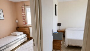 Ein Hotelzimmer mit zwei Betten, einem kleinen Tisch, einem Sessel, einer Lampe und einem Fenster mit Vorhängen.