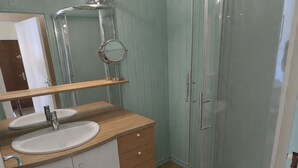 Ein Badezimmer mit Duschkabine aus Glas, einem Waschbecken mit Spiegel darüber und Holzschränken.