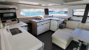 A compact galley with a stove, sink, and seating area, overlooking a marina. - Sun-Kissed Sailing Adventure in Zadar, Croatia (Biograd na moru)