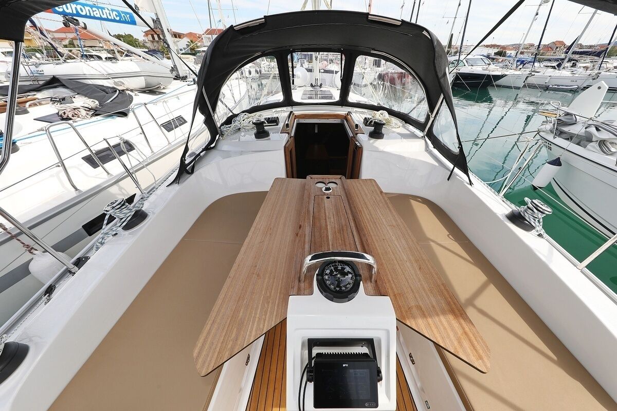 A boat deck with a central wooden table, a steering wheel, and a view of other boats in the marina.