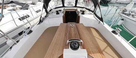 A boat deck with a central wooden table, a steering wheel, and a view of other boats in the marina.