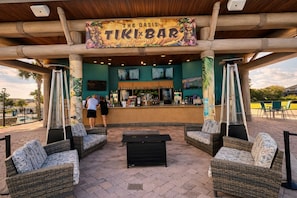 Un bar tiki a l'aire lliure amb mobles de vimetla, una barra i un cartell que diu 'The Oasis TIKI BAR'.