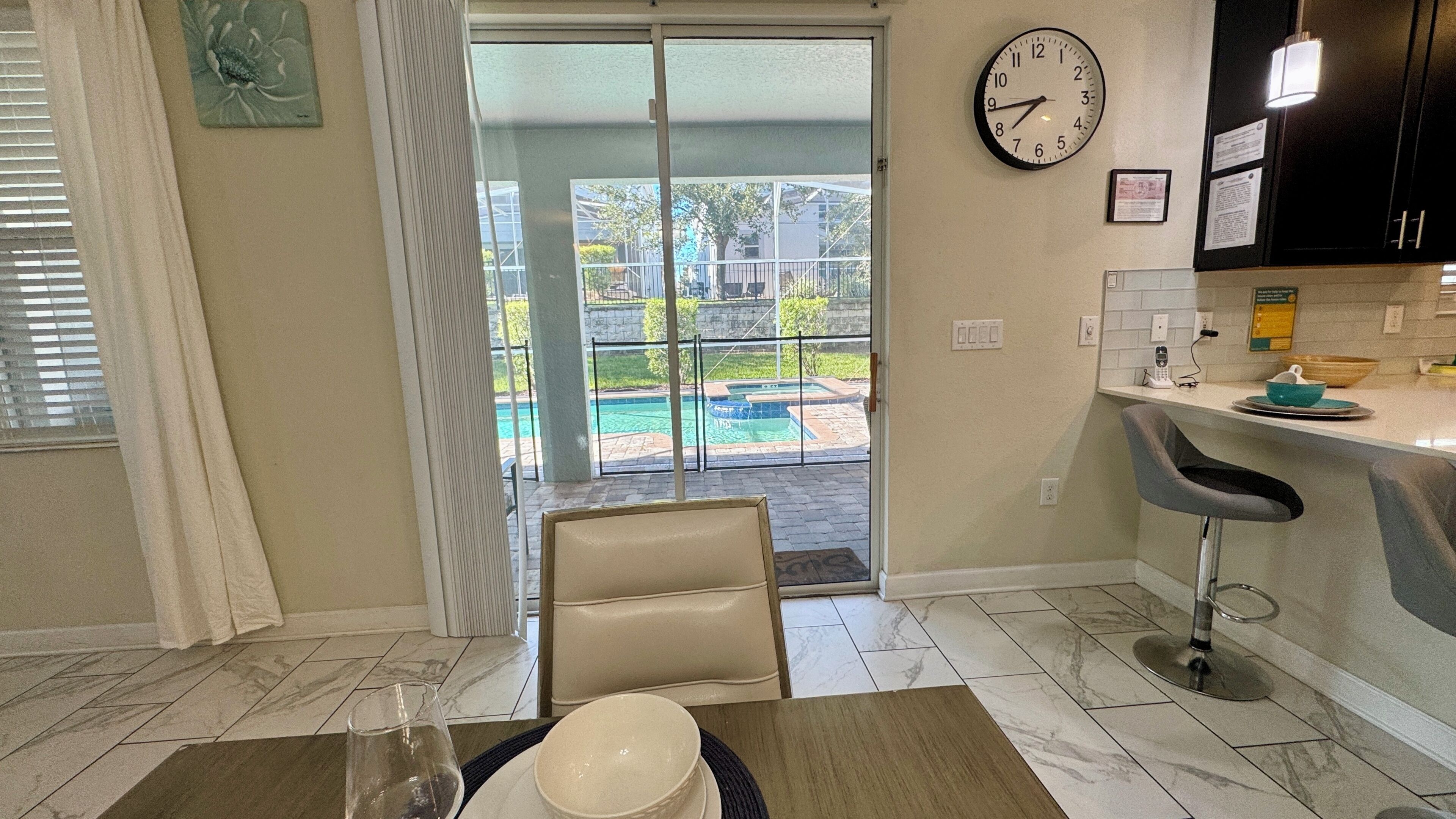 A kitchen with a clock, a bar area, and a view of a swimming pool.