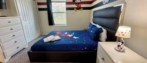 A bedroom with a bed, dresser, nightstand, and a Mickey Mouse wall decal.