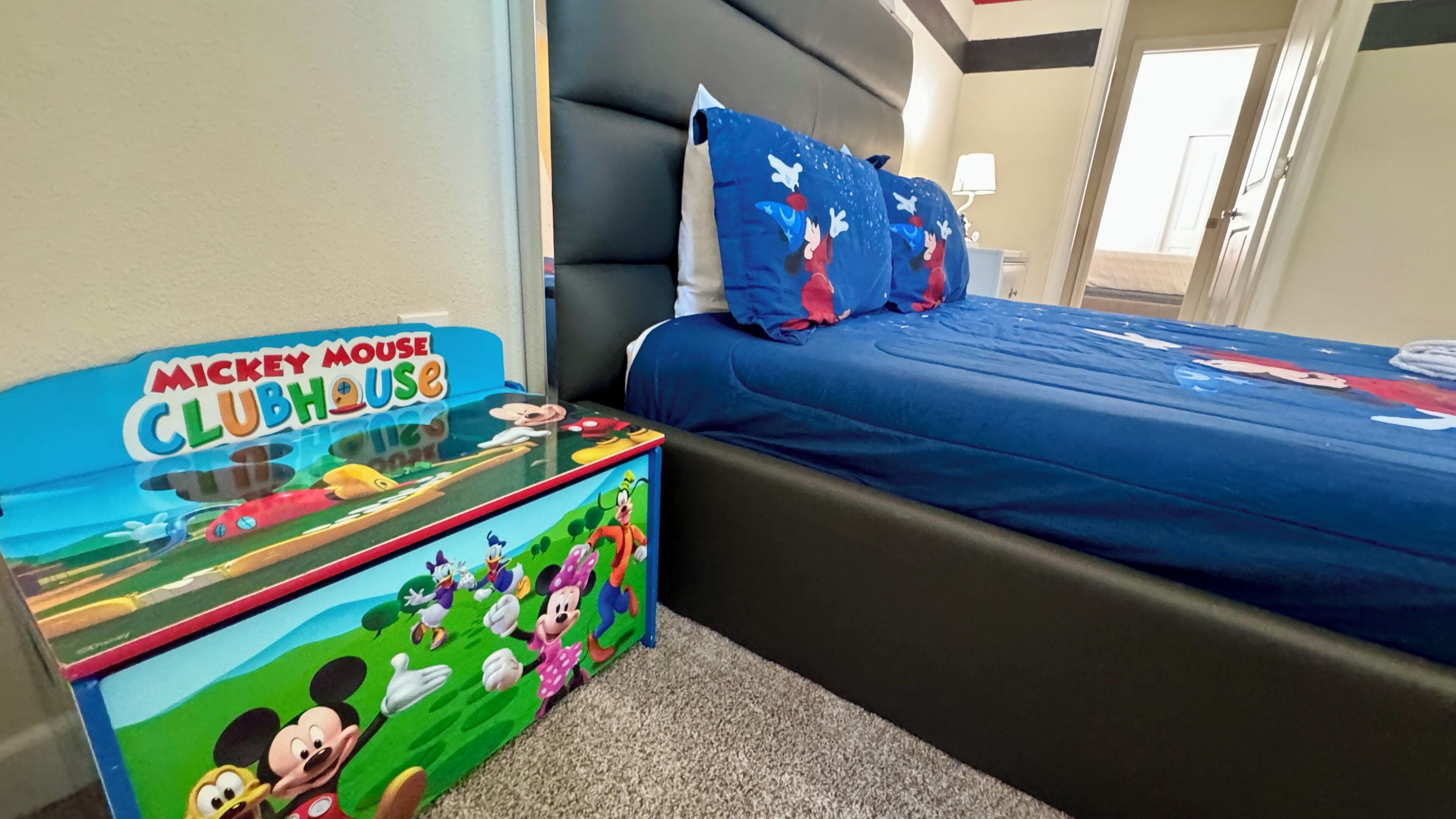 A hotel room with a Mickey Mouse Clubhouse themed table, a bed with blue bedding, and a nightstand.