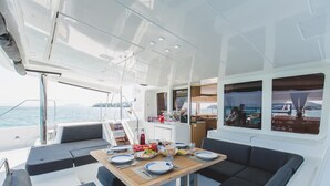 L’espace repas d’un yacht, avec une table dressée pour deux personnes, un canapé et une vue sur la mer.