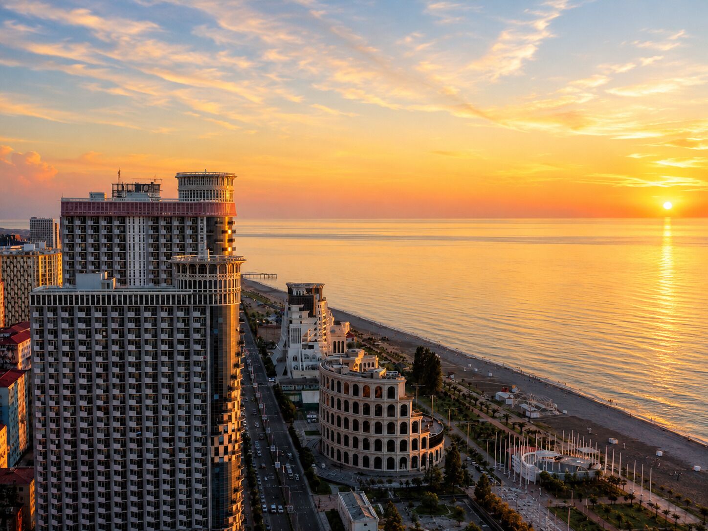 A coastal cityscape with high-rise buildings, a curved architectural structure, and a beach.